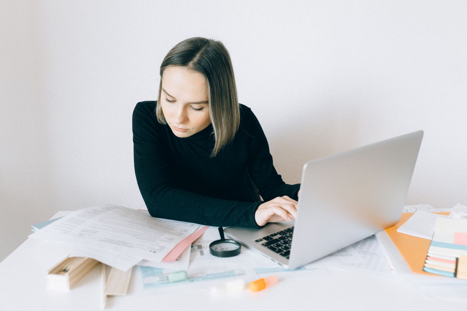 Žena pri notebooku porovnáva papierové podklady počas kontroly dokumentu
